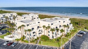A beachfront hotel with multiple-story buildings, parking, and a view of the ocean.