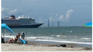 A beach with a cruise ship in the background, people swimming, and a large blue structure on the shore.