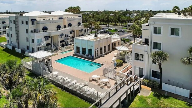 A modern hotel with a swimming pool, multiple balconies, and a well-maintained lawn.