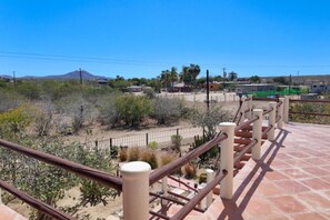 A balcony with a tiled floor, metal railing, and a view of a desert landscape with sparse vegetation and distant buildings. - Ocean & Mountain View Terrace in La Capilla (Buena Vista)