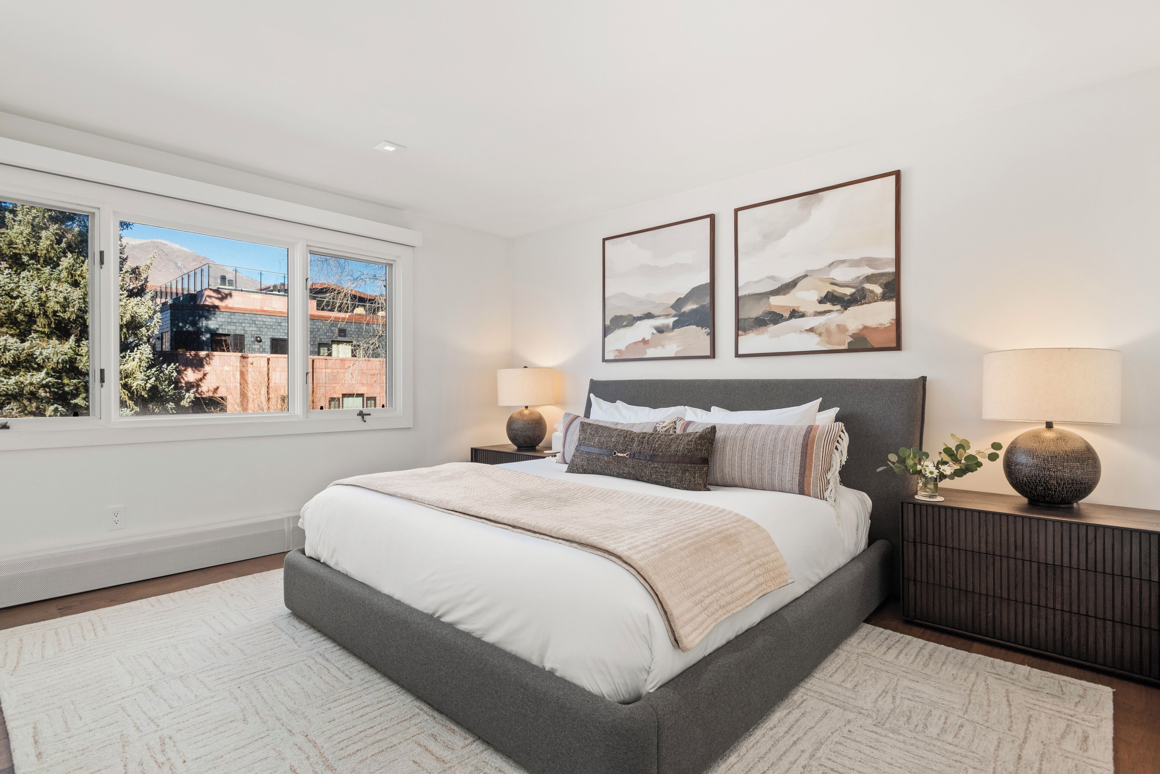 A bedroom with a large bed, two bedside tables, a window with a view, and two wall-mounted artworks.