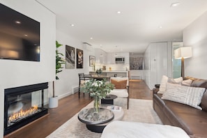 A modern living room with a fireplace, a dining area, and a kitchen in the background.