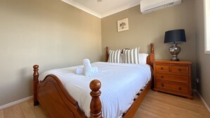 A bedroom with a wooden bed, a nightstand, a lamp, and an air conditioning unit. - Family-Friendly 3BR Home Near Calamvale Central (Calamvale)