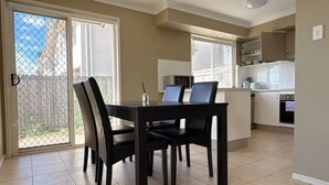 A dining area with a table and chairs, a kitchen with cabinets and appliances, and a sliding glass door leading to a patio. - Family-Friendly 3BR Home Near Calamvale Central (Calamvale)