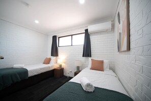 Habitación con dos camas, una ventana con cortinas, un equipo de aire acondicionado y una obra de arte colgada en la pared.