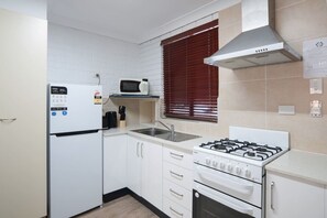 Una cocina compacta con refrigerador, microondas, lavaplatos, estufa y alacenas.