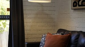 Una sala de estar con un sofá de cuero negro, una pared de ladrillo blanco y una lámpara de pie negra.