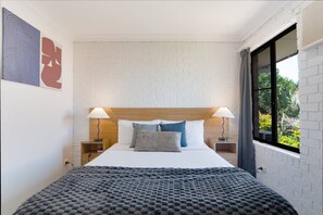 Une chambre d’hôtel avec un lit, deux lampes de chevet, une fenêtre donnant sur un paysage agréable et un mur à motifs.
