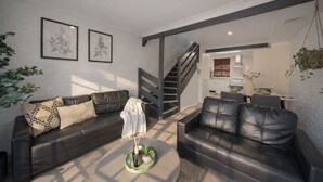 Ein modernes Wohnzimmer mit zwei Ledersofas, einem Couchtisch mit Pflanzen, einer Treppe und einer Küche im Hintergrund.
