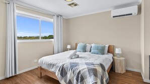 Een slaapkamer met een bed, bedlampen, een airconditioning en een raam met gordijnen.