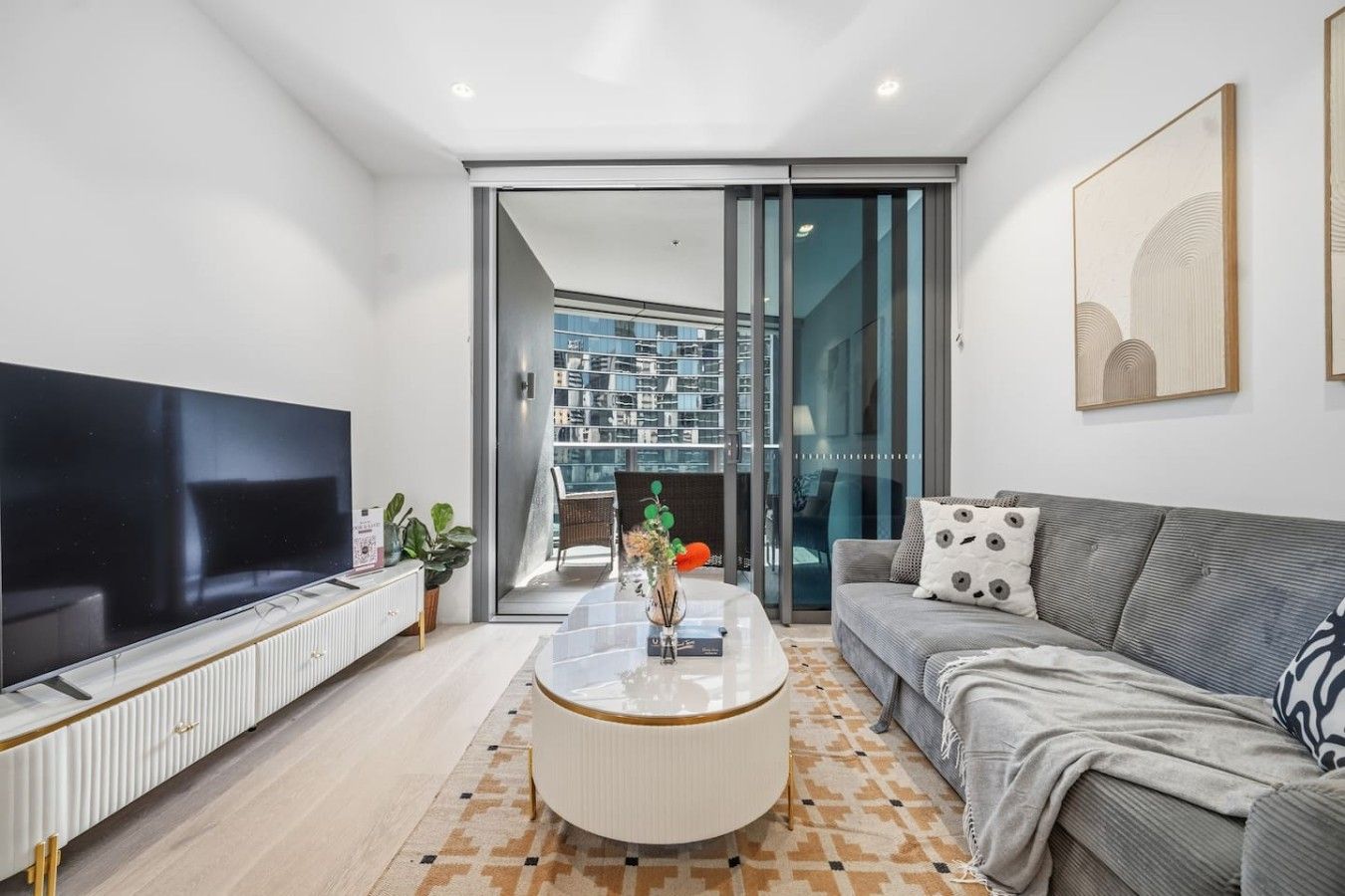 Een moderne woonkamer met een flatscreen televisie, een bank, een salontafel en een schuifpui naar een balkon.