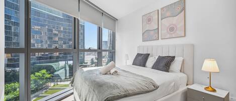 A modern bedroom with a large window, a bed, a nightstand, and two wall art pieces.