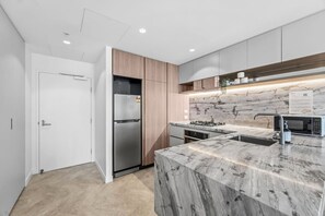 A modern kitchen with a built-in refrigerator, a gas stove, and a marble countertop. - Luxury 54F Skyline Apt | Iconic Queen’s Wharf 1BR (Brisbane City)