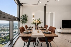 A modern dining room with a city view, a large dining table set for six, and a television in the corner. - Luxury 54F Skyline Apt | Iconic Queen’s Wharf 1BR (Brisbane City)