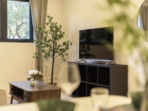 Una sala de estar con televisor, una planta y una pequeña mesa con un florero.