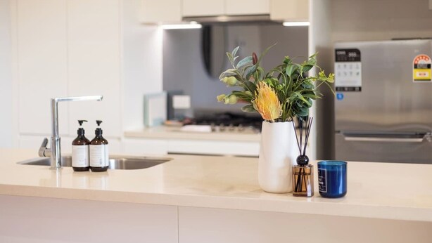 Uma cozinha moderna com geladeira de aço inoxidável, pia com dosadores de sabão e um vaso com flores na bancada.