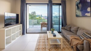 Uma sala de estar moderna com televisão de tela plana, um sofá, uma mesa de centro e uma varanda com vista.