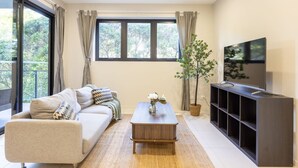 A modern living room with a sofa, coffee table, TV stand, and a large window with curtains. - Modern 2BR | Ducted A/C, Parking & Great Location (MacGregor)