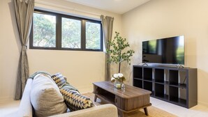 A living room with a sofa, a coffee table, a TV, and a bookshelf. - Modern 2BR | Ducted A/C, Parking & Great Location (MacGregor)