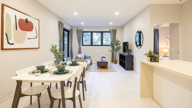 A modern living room with a dining area, a sofa, a coffee table, and a TV. - Modern 2BR | Ducted A/C, Parking & Great Location (MacGregor)