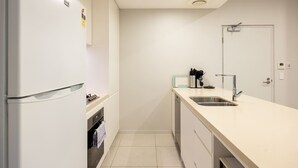 A compact kitchen with a refrigerator, sink, and cabinets. - Modern 2BR | Ducted A/C, Parking & Great Location (MacGregor)