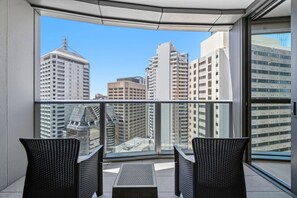 A balcony with two chairs and a table, overlooking a cityscape with tall buildings. - Landmark Queens Wharf 1BR w/ Pool, Gym & City View (Brisbane City)