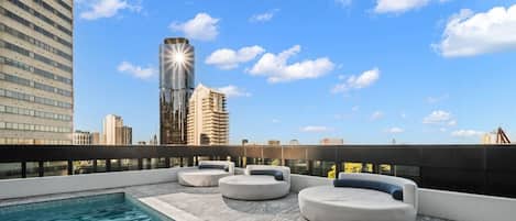 Terraço no terraço com piscina e áreas de estar, com vista para um horizonte urbano repleto de edifícios modernos.