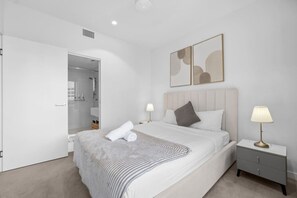 A modern bedroom with a large bed, bedside tables, a nightstand, a walk-in closet, and abstract wall art. - Landmark Queens Wharf 1BR w/ Pool, Gym & City View (Brisbane City)