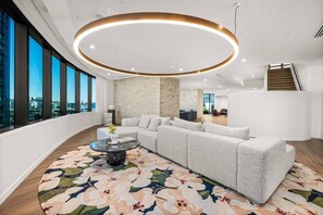 A modern living room with a sectional sofa, a round coffee table, and a large window offering a city view. - Landmark Queens Wharf 1BR w/ Pool, Gym & City View (Brisbane City)