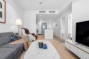 A modern living room with a sofa, a massage chair, a coffee table, and a TV. - Landmark Queens Wharf 1BR w/ Pool, Gym & City View (Brisbane City)