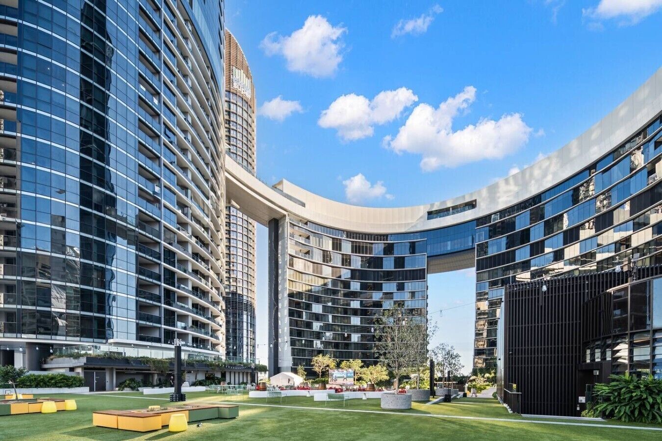 A modern hotel with a curved glass facade, outdoor seating areas, and a well-maintained lawn.