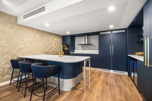 Cozinha moderna com ilha central, banquetas e armários escuros.