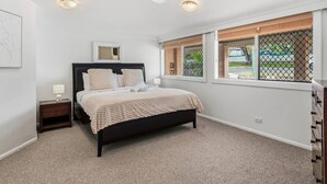 Un dormitorio con cama, mesita de noche, ventilador de techo y ventanas con vistas al exterior.