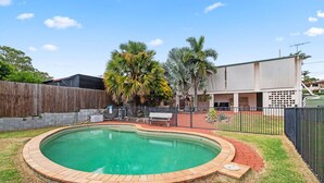 Un patio trasero con piscina, cerca de madera y un edificio de techo plano.