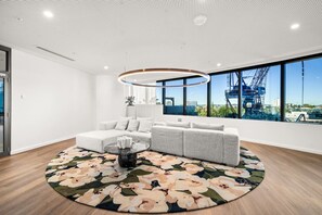 Ein modernes Wohnzimmer mit einer Eckcouch, einem runden Couchtisch und einem großen Fenster mit Blick auf Baukräne.