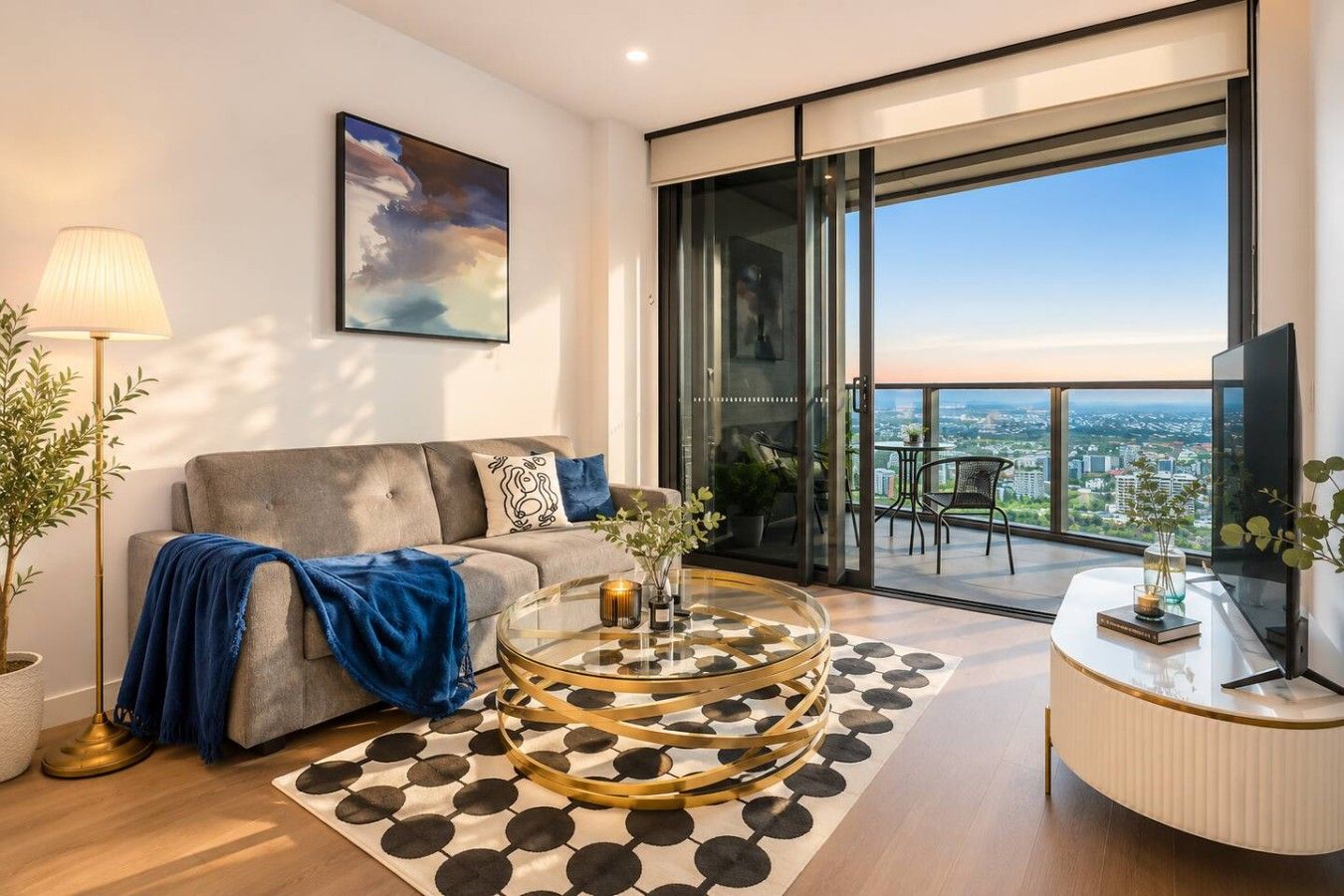 A modern living room with a sofa, a round coffee table, and a large window offering a city view.