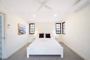 Un dormitorio con una cama grande, dos mesitas de noche, un ventilador de techo y un cuadro en la pared.