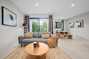 A modern living room with a grey sofa, a round wooden coffee table, and a dining area with a wooden table and chairs. - Southside 2BR Apt Near Garden City & Sunnybank (MacGregor)