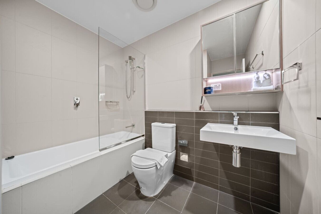 A modern bathroom with a glass-enclosed shower, a white toilet, and a sink with a mirror above it.