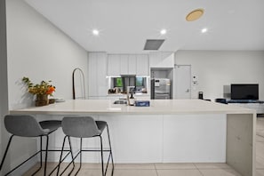 A modern kitchen with a central island, bar stools, and a built-in refrigerator. - Southside 2BR Apt Near Garden City & Sunnybank (MacGregor)