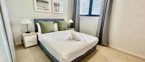 A neatly made bed with a white comforter and pillows, a bedside lamp, and a nightstand with a lamp.