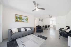 A modern living room with a gray sofa, black armchairs, a dining area with a table and chairs, and a ceiling fan. - Budget-Friendly | Lock-Up Garage | Near Everything (New Farm)