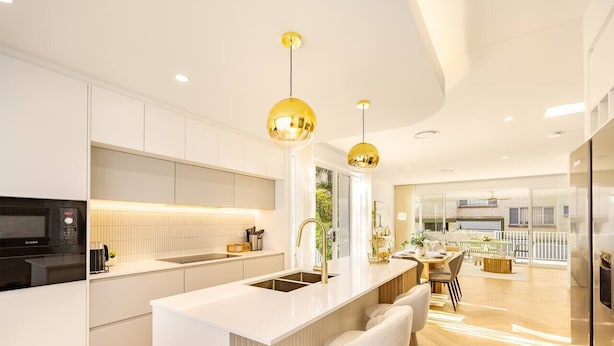 A modern kitchen with a central island, bar stools, and pendant lighting. - Brand-New 4BR Luxury Living Near Airport & Mall (Nundah)