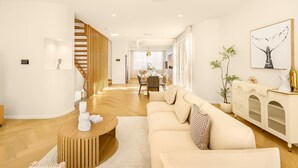 A modern living room with a sofa, a coffee table, and a dining area in the background. - Brand-New 4BR Luxury Living Near Airport & Mall (Nundah)