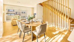 A modern dining area with a wooden table, chairs, and a view of the outside. - Brand-New 4BR Luxury Living Near Airport & Mall (Nundah)