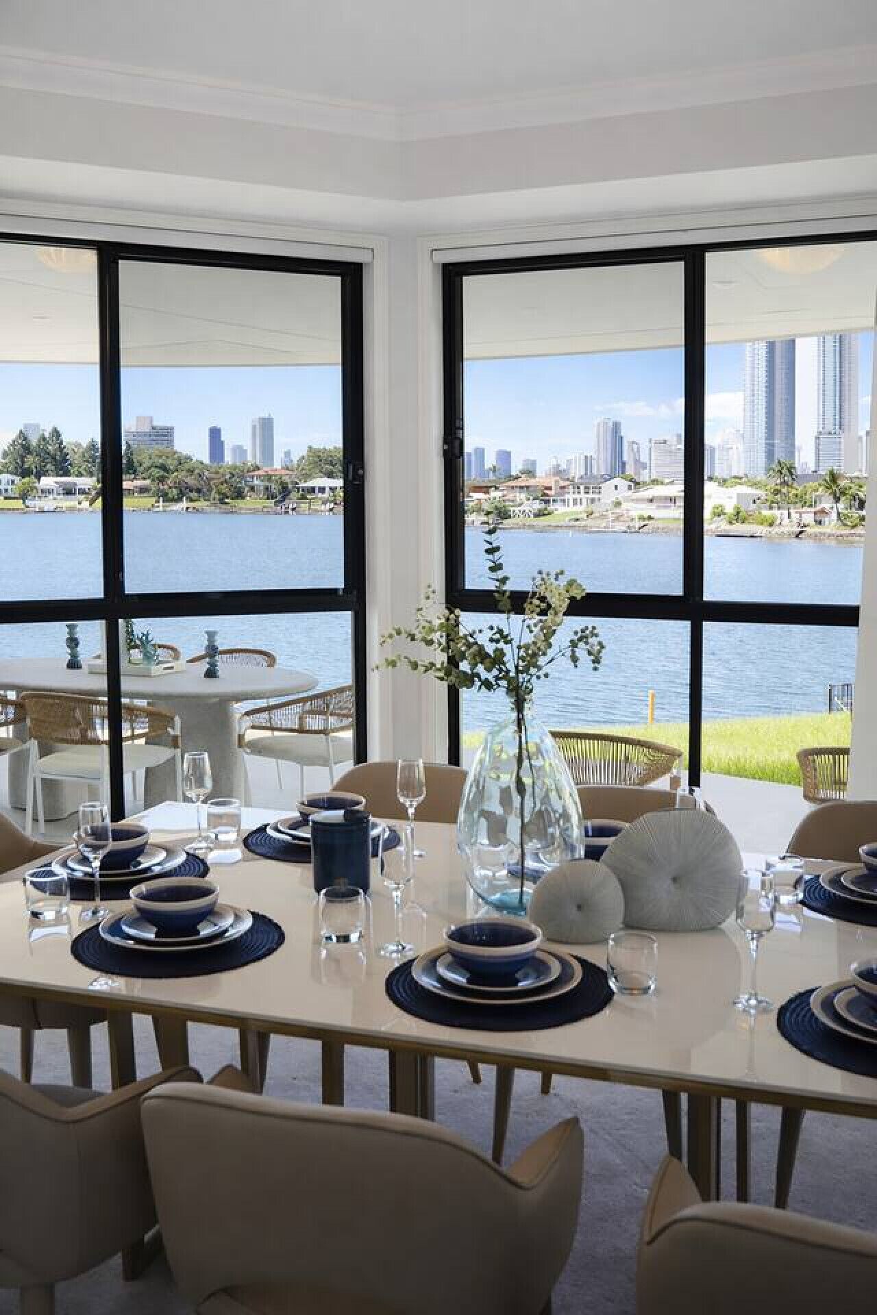 A dining area with a table set for four, large windows with a cityscape view, and a water body in the background.