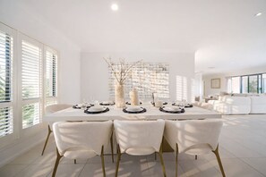 Une salle à manger moderne avec une table blanche dressée pour quatre personnes, des chaises blanches et un vase décoratif.