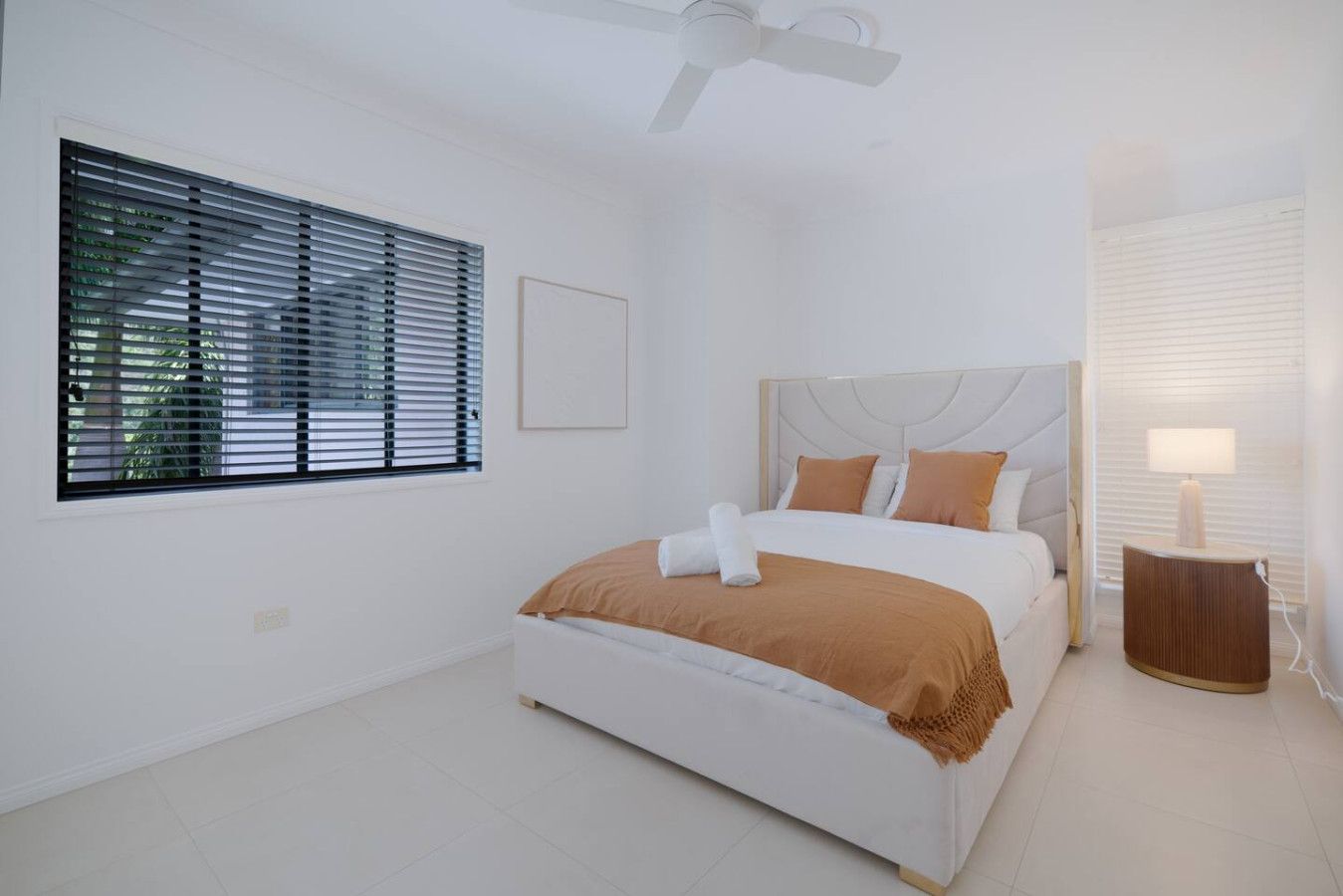 A bedroom with a bed, a ceiling fan, a bedside lamp, and a window with blinds.