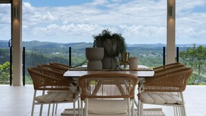 Ein Essbereich mit Tisch und Stühlen, einer großen Topfpflanze und Blick auf eine gebirgige Landschaft.