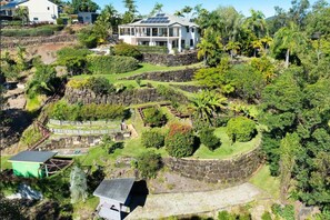 Una casa grande con techo solar, rodeada de abundante vegetación y muros de piedra.
